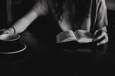 在黑色陶瓷杯旁的桌子上，一位女士正在看书的灰度照片